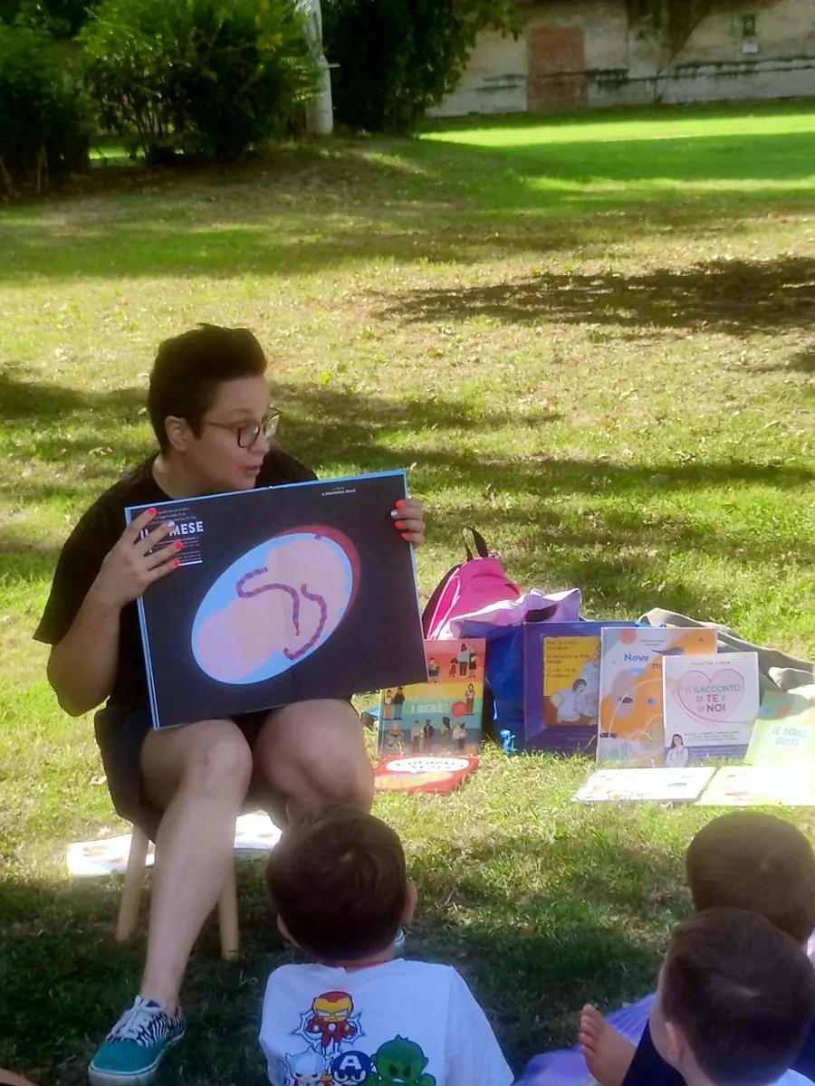 Beatrice legge un albo illustrato sulla gravidanza a un gruppo di bambini in un parco